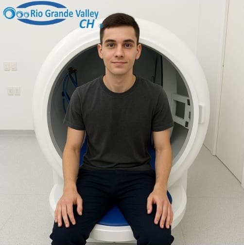 Joven paciente sentado en la entrada de una cámara hiperbárica en sala médica blanca, listo para tratamiento de oxigenación hiperbárica.